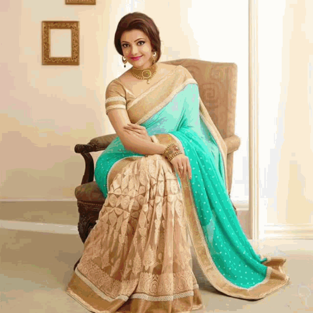 a woman is sitting in a chair wearing a turquoise and gold saree