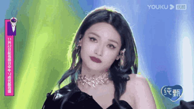 a woman wearing a necklace and earrings looks at the camera with a youku logo behind her
