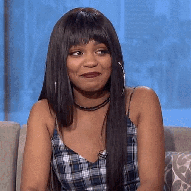 a woman is sitting on a couch wearing a plaid top and hoop earrings .