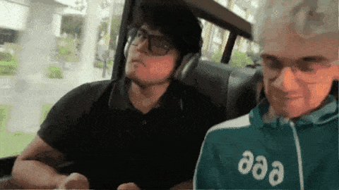 a man wearing headphones is sitting next to another man wearing a green jacket with the word aaa on it .