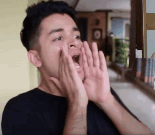 a man in a black shirt is shouting with his hands in front of his mouth