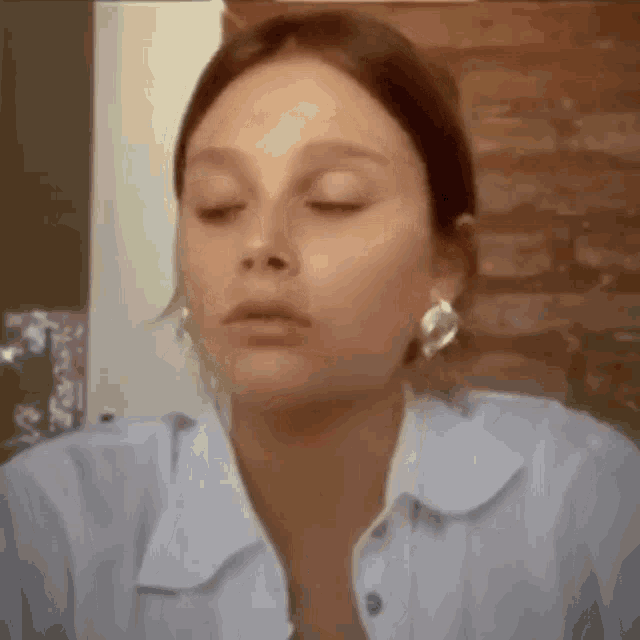 a close up of a woman 's face with her eyes closed . she is wearing earrings and a white shirt .