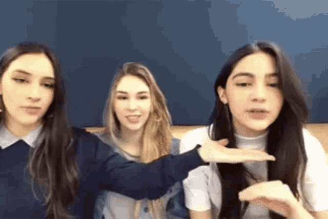 three girls are sitting next to each other on a couch and talking to each other .