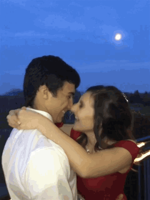 a man and a woman are hugging and kissing with the moon in the background