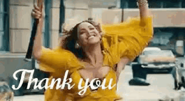 a woman in a yellow dress is dancing in the street with her arms in the air and the words `` thank you '' written below her .