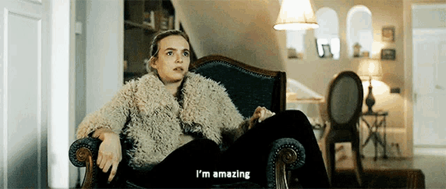 a woman in a fur coat is sitting in a chair saying i 'm amazing