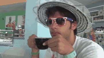 a man wearing sunglasses and a hat is drinking from a cup