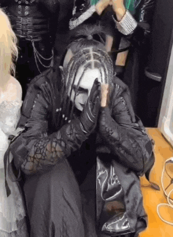 a man in a gothic costume is sitting on a wooden floor with his hands folded in prayer .