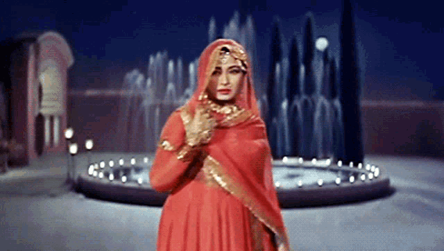 a woman in a red dress stands in front of a water fountain