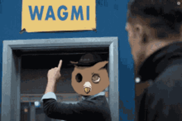 a man wearing an owl mask is giving the middle finger in front of a sign that says wagmi
