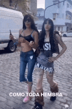 two women standing next to each other on a cobblestone street with the words como toda hembra written on the bottom