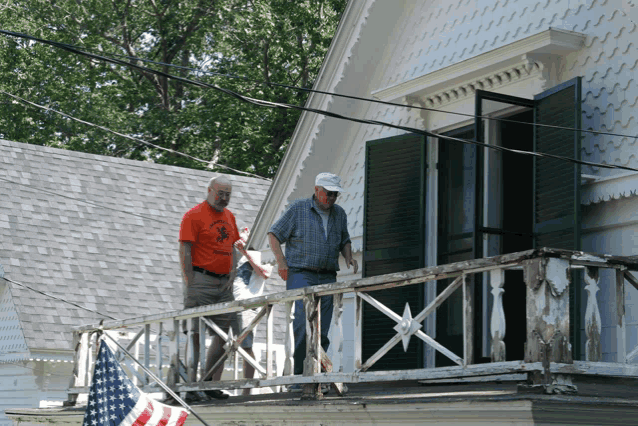 two men standing on a balcony with an american flag in the background