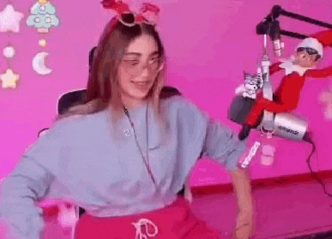 a girl is dancing in front of a microphone in a pink room with an elf on the shelf in the background .