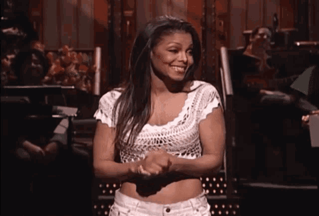 a woman in a white crop top and white shorts smiles for the camera