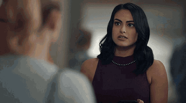 a woman in a purple top and necklace is talking to another woman