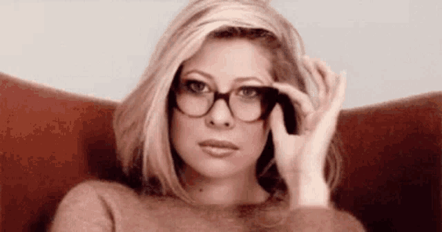 a woman wearing glasses is sitting in a chair with her hand on her face .