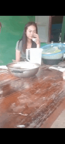 a woman is sitting at a table with a bowl of food and drinking from a pitcher .