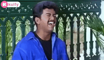 a man in a blue shirt is laughing while sitting in front of a railing .