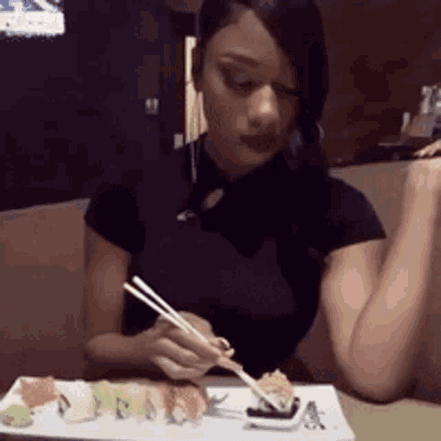 a woman is eating sushi with chopsticks from a white plate