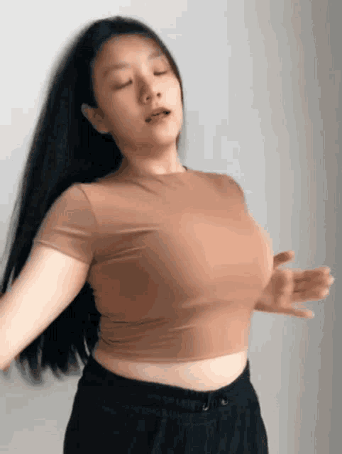 a woman in a brown crop top and black shorts is dancing with her eyes closed