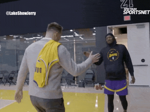 a man wearing a lakers sweatshirt shakes hands with another person