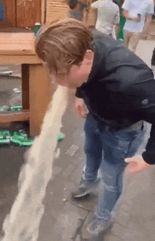 a man is throwing up on the sidewalk in front of a crowd