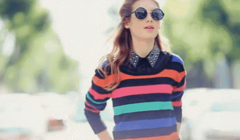 a woman wearing a colorful striped sweater and round sunglasses