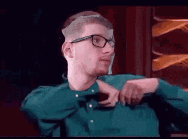 a man wearing glasses and a green shirt is sitting in front of a mirror .