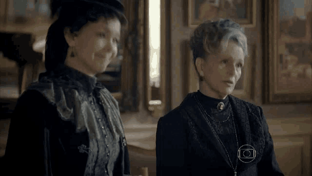 two women are standing next to each other in a room and talking to each other .