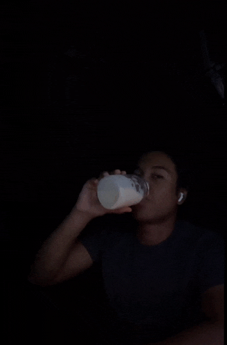 a man wearing a black shirt and ear buds looks at the camera in the dark