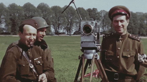 three men in military uniforms are standing in a field with a camera