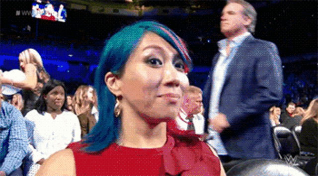 a woman with blue hair is sitting in a stadium with a man in a suit .