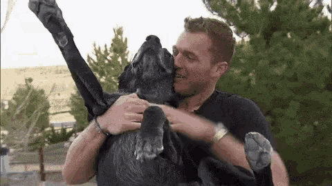 a man in a black shirt is holding a black dog