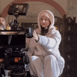 a woman in a hooded jacket is kneeling down in front of a camera .