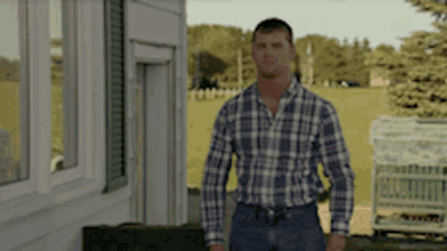 a man in a plaid shirt is standing in front of a white building