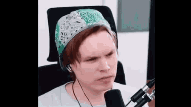 a man wearing a bandana and headphones is sitting in front of a microphone and making a funny face .