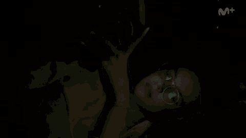 a person wearing glasses is laying down in the dark looking at their cell phone .