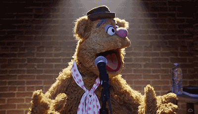 muppet fozzie bear singing into a microphone with a brick wall in the background