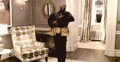 a man wearing a tool belt is standing in a living room next to a chair .