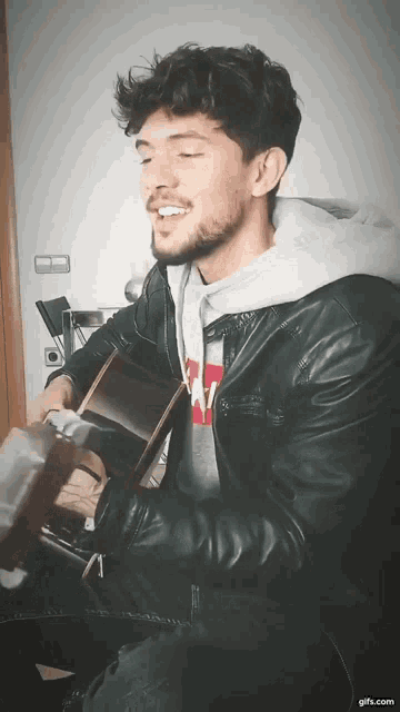 a man in a leather jacket is playing a guitar and singing