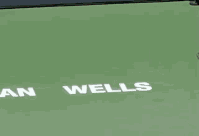 a man in an orange shirt is holding a tennis racquet on a tennis court that says wells