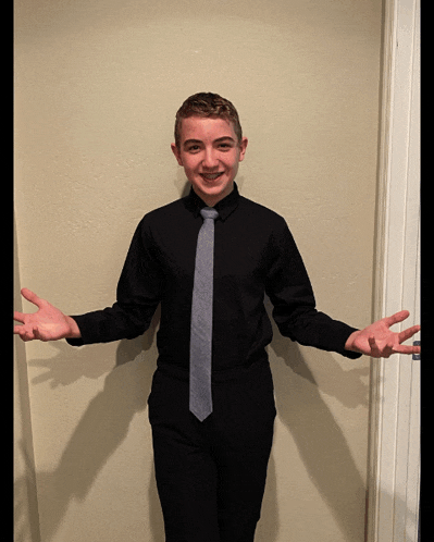 a young man in a black shirt and tie is standing in front of a wall