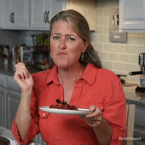 a woman in a red shirt is eating a plate of food with #plantbased written on the bottom
