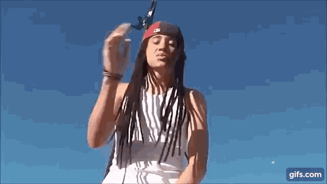 a man with dreadlocks and a bandana on his head is standing in front of a blue sky holding a toy airplane .