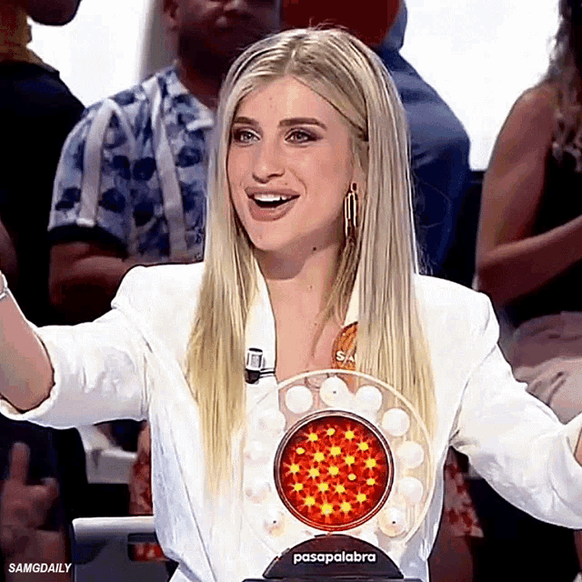 a woman in a white jacket is smiling in front of a prize that says pasapalabra