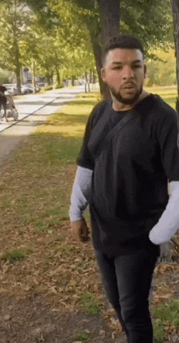 a man in a black shirt is standing in a park looking at the camera