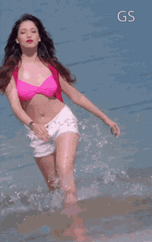 a woman in a pink bikini and white shorts is running in the ocean .
