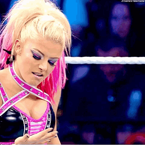 a woman with pink hair is standing in a wrestling ring and looking down .