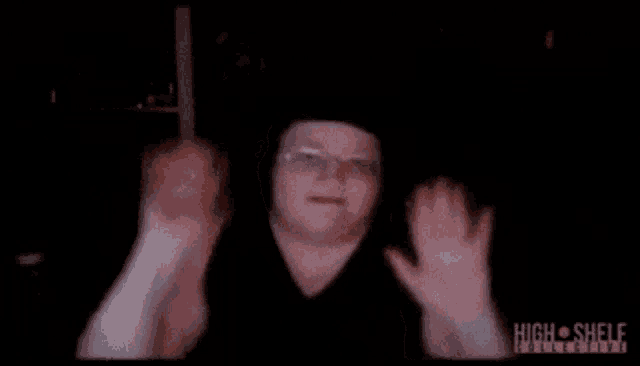 a man with glasses and a black shirt is waving his hands in front of a screen that says high shelf