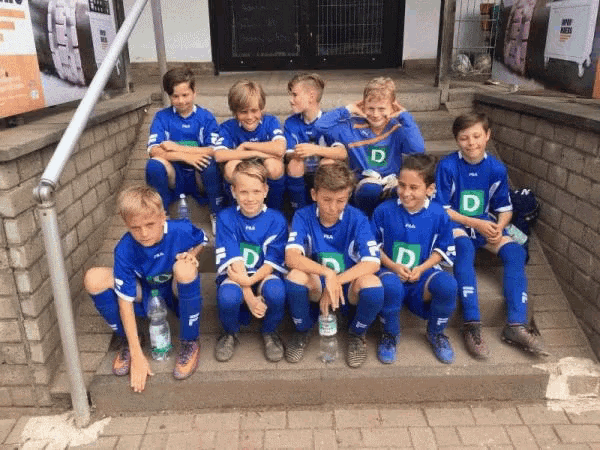 a group of young boys wearing blue shirts with the letter d on them sit on a set of stairs